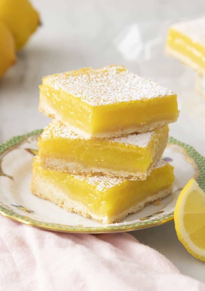 Lemon bars dusted with powdered sugar on a green and white plate.