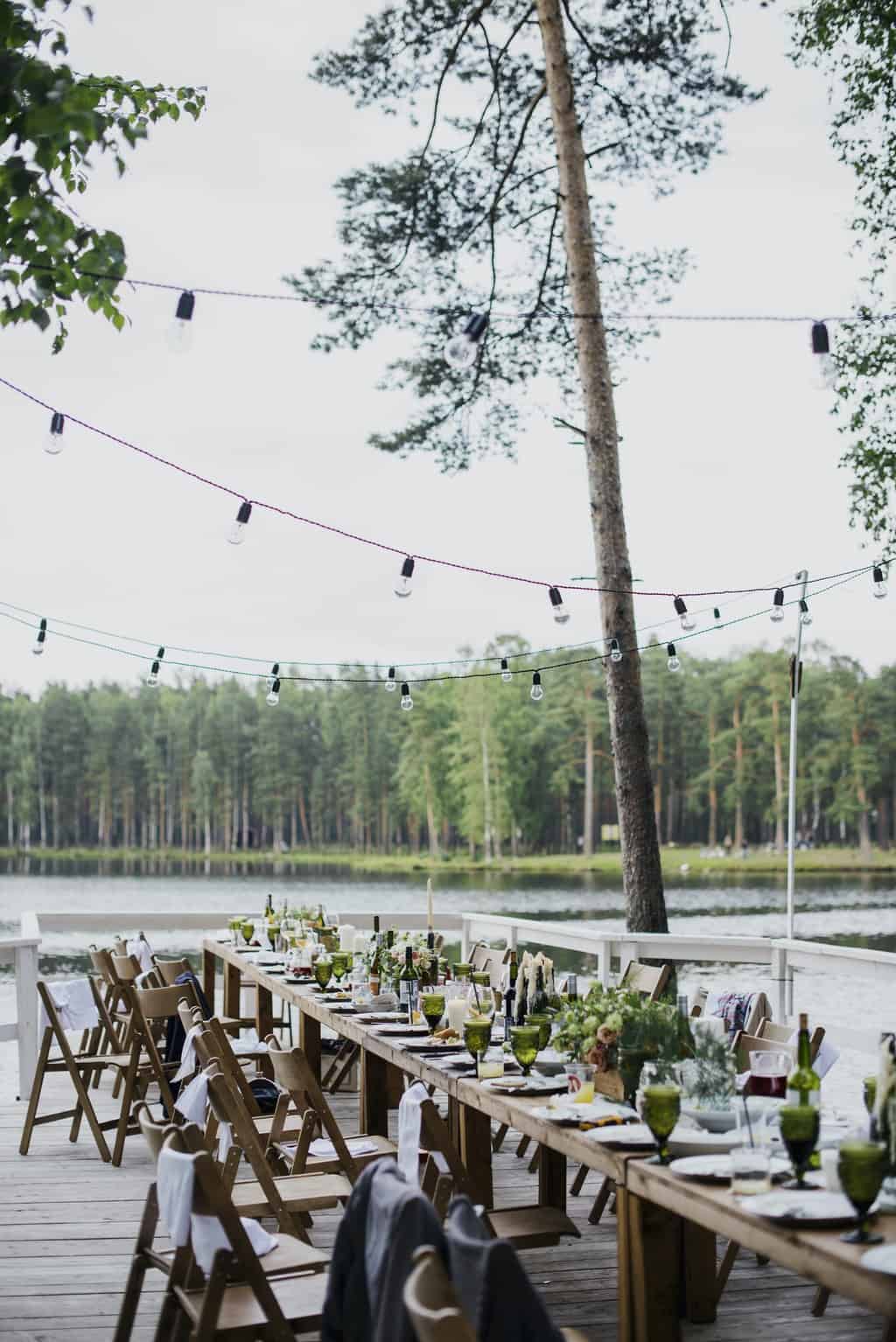 Free Wooden terrace with green trees and tables located near lake preparing for festive romantic party in nature under blue sky Stock Photo