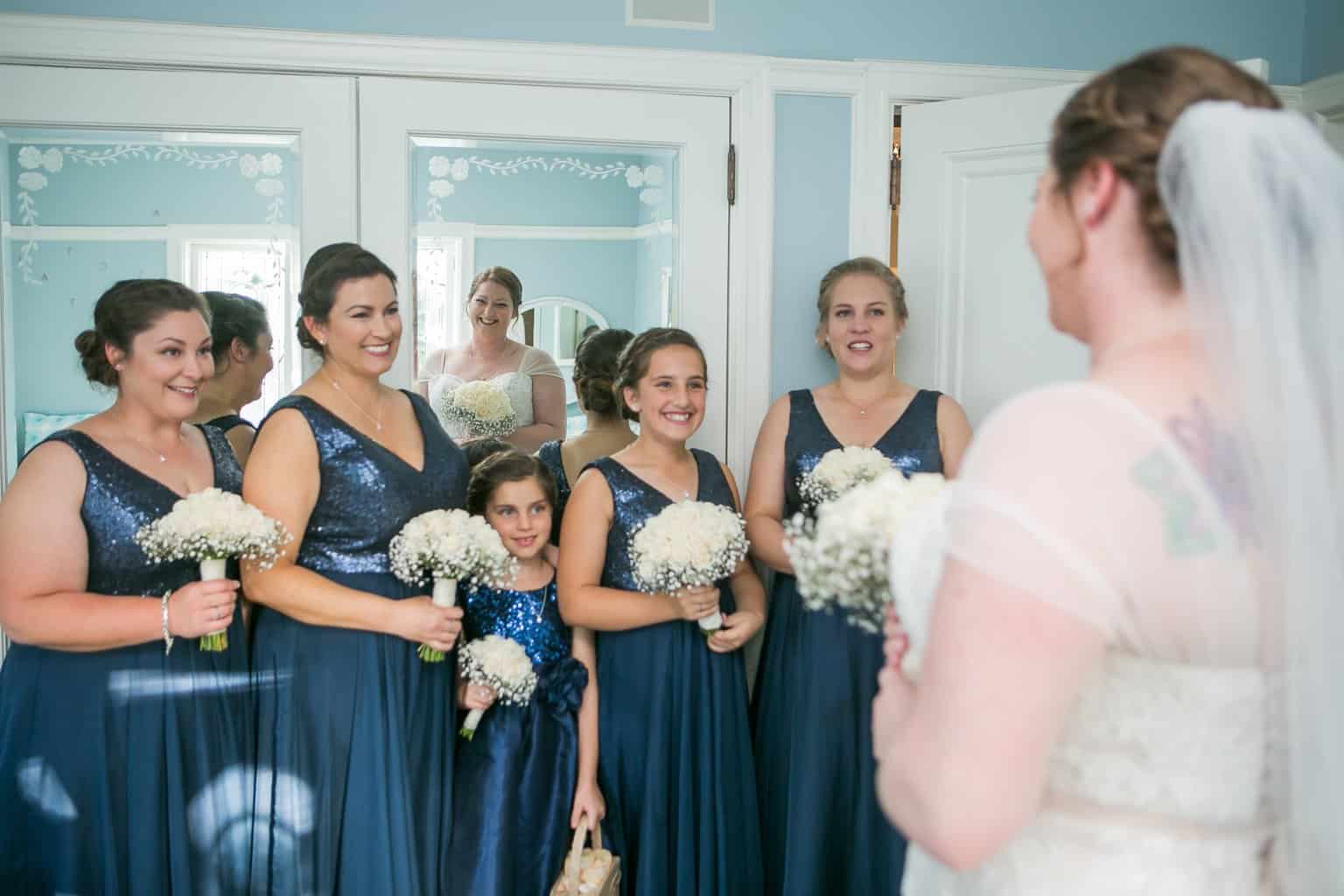 Free Happy bridesmaids of different ages in similar elegant dresses smiling while standing in room with flower bouquets and congratulating joyful bride Stock Photo