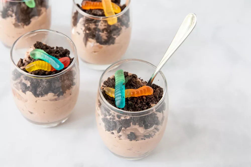 Chocolate dirt pudding topped with chocolate cookie crumbles and gummy worms in individual glass cups