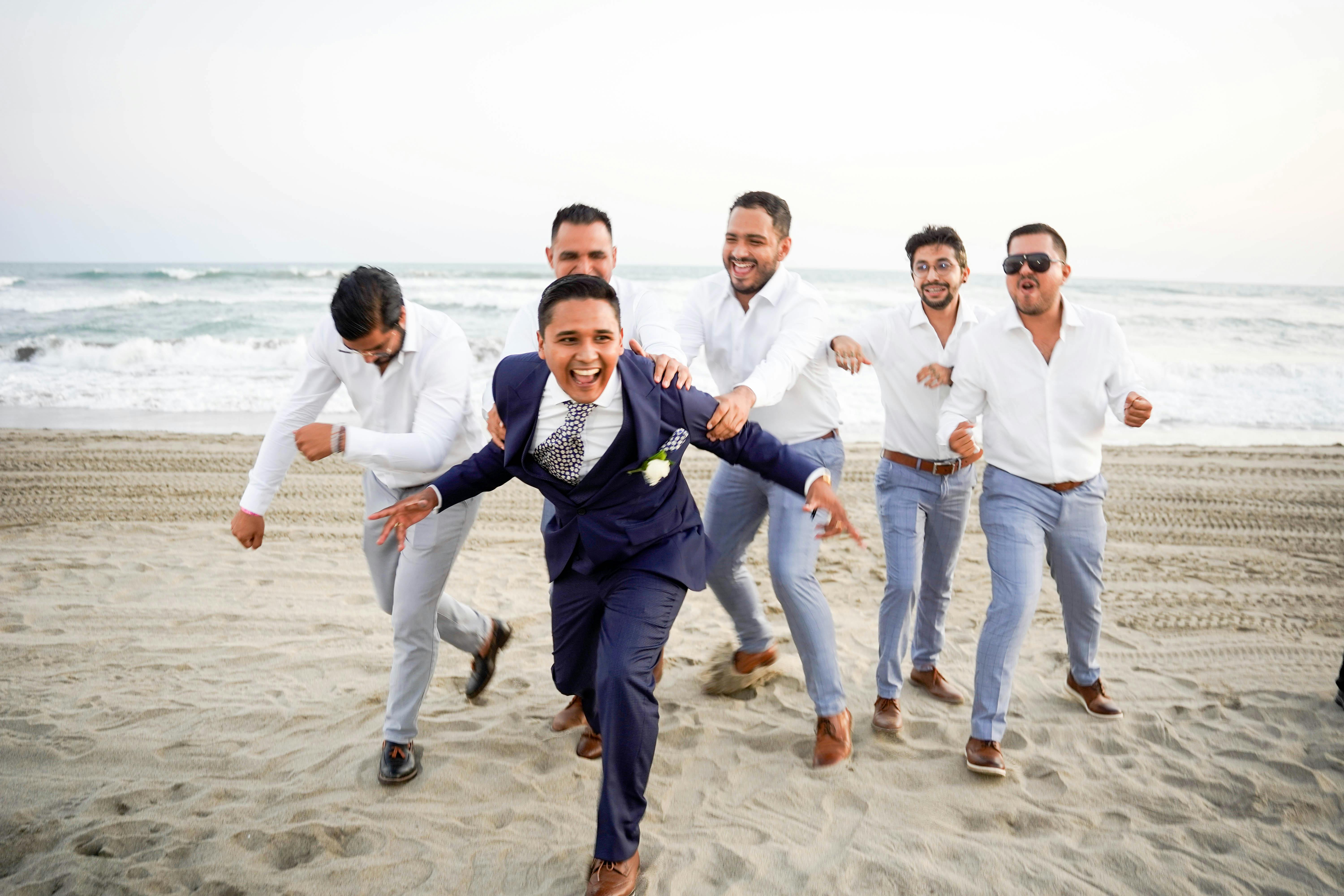 Groomsmen Attire Tips for All Types of Destination Weddings 9 Free A joyful moment of a groom and his groomsmen running on a sandy beach during a wedding. Stock Photo