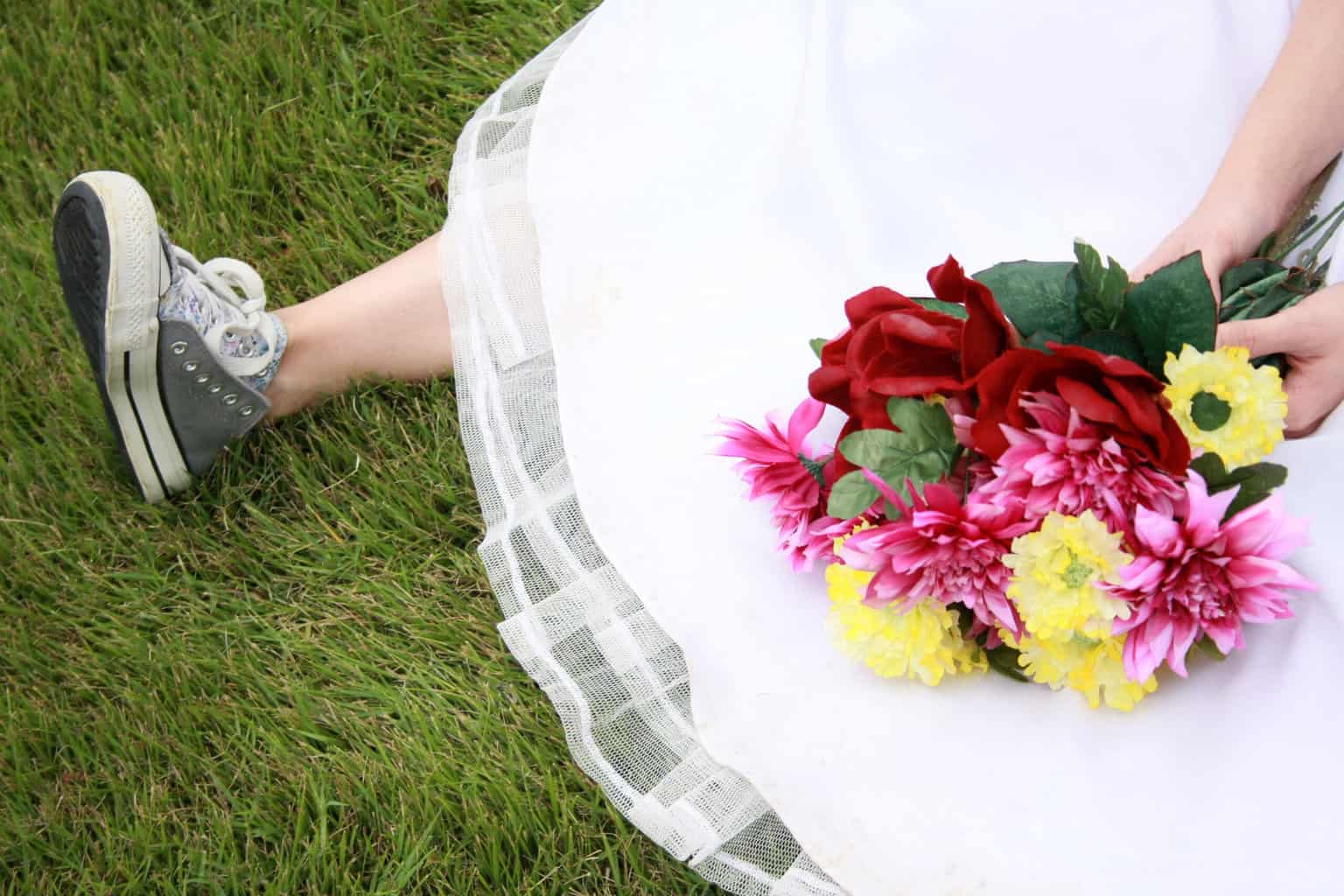 Bride sitting on grass in wedding dress wearing gray Converse