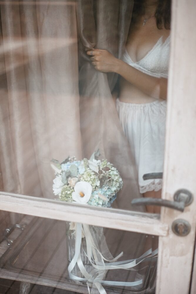 Free Woman in White Lingerie Standing Behind the Curtain Near Bouquet with Ribbons Stock Photo