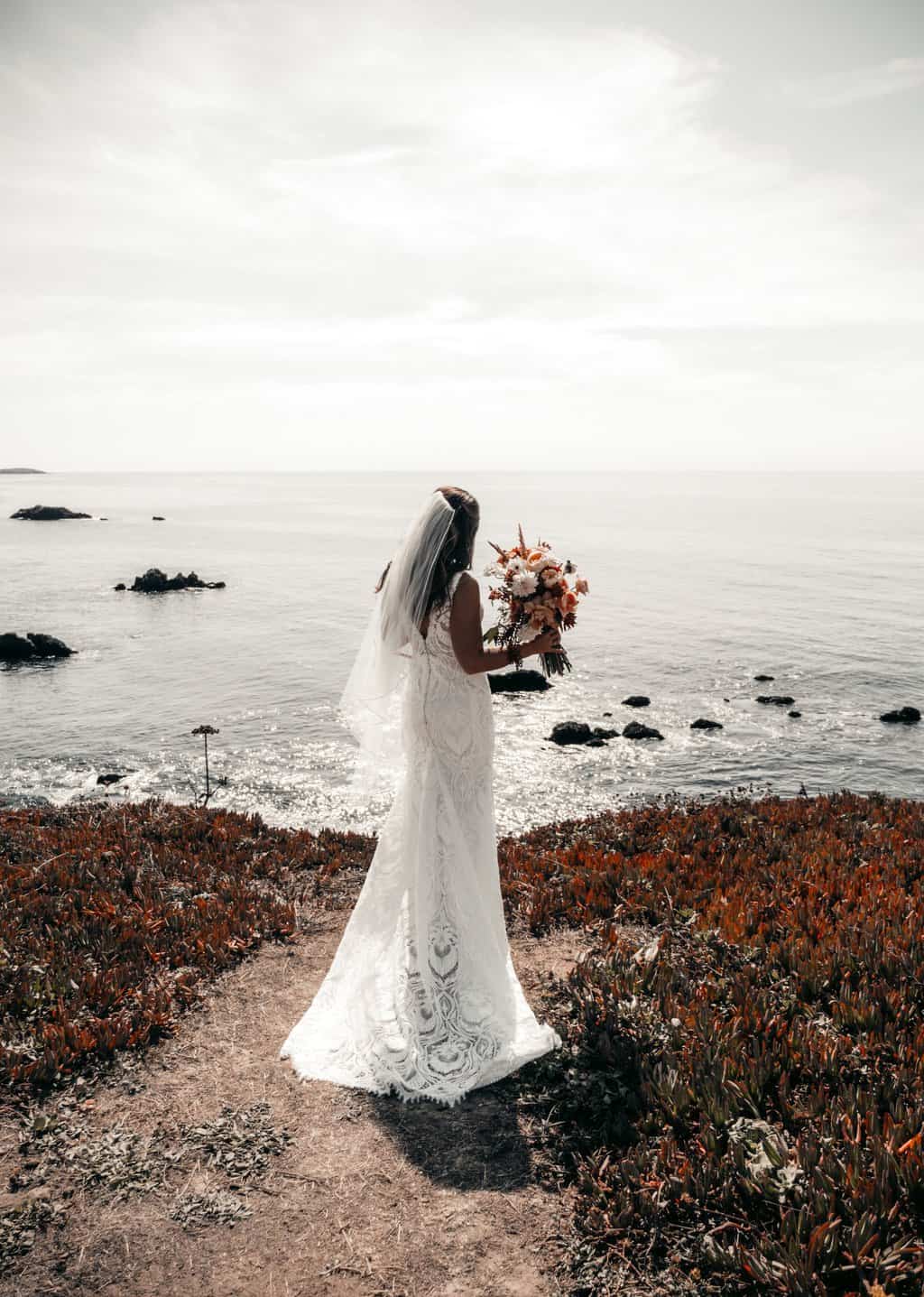 woman in white wedding dress standing on rocky shore during daytime
